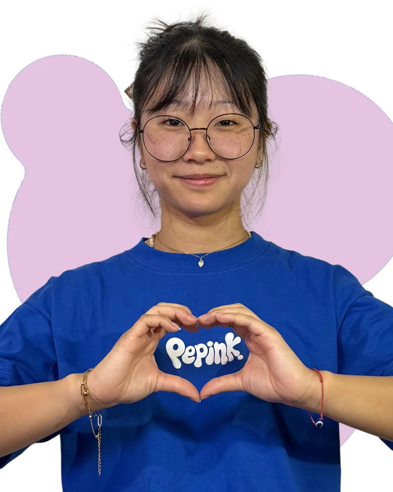 Mica formando un corazón con las manos sobre el logo de su remera azul de Pepink, recortada sobre una mancha rosa